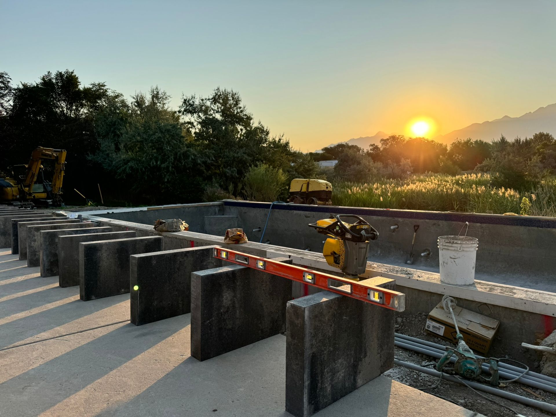 Concrete blocks and a level tool at a construction site overlooking a sunset over trees and mountains.