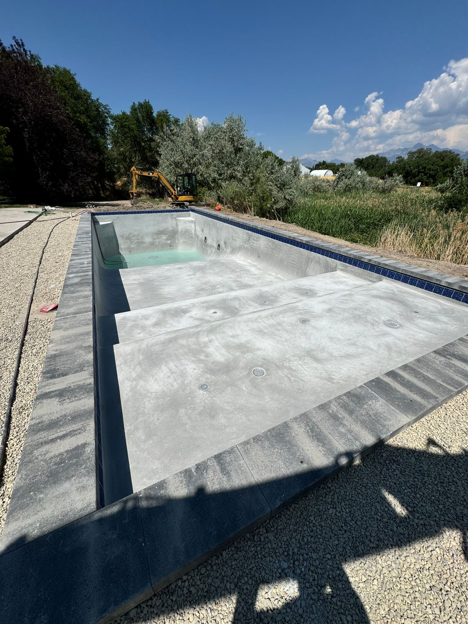 A partially filled rectangular swimming pool under construction, surrounded by light-colored gravel and dark stone coping.