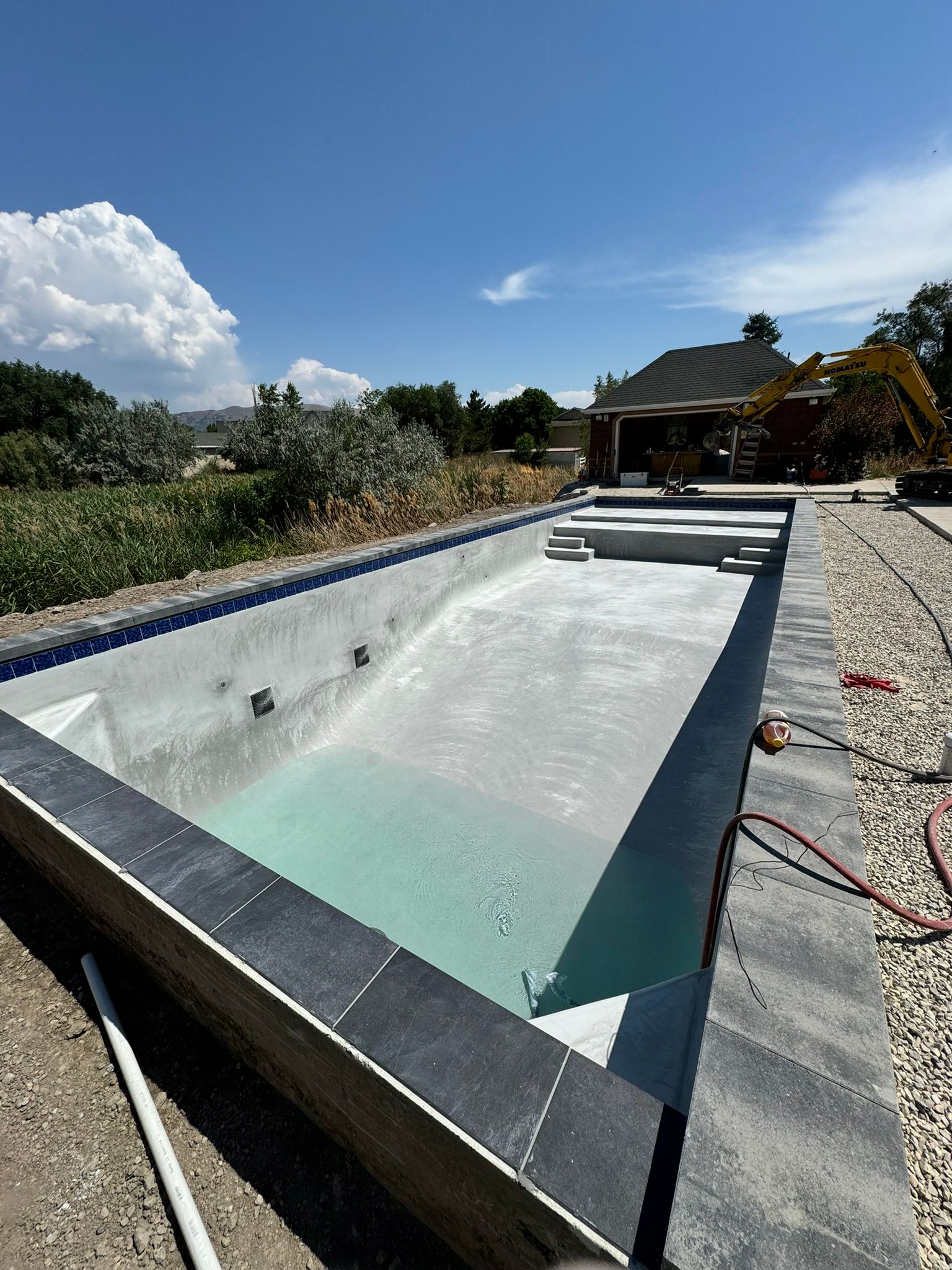 An empty rectangular swimming pool under construction, featuring gray tile borders and light-colored plaster finish.