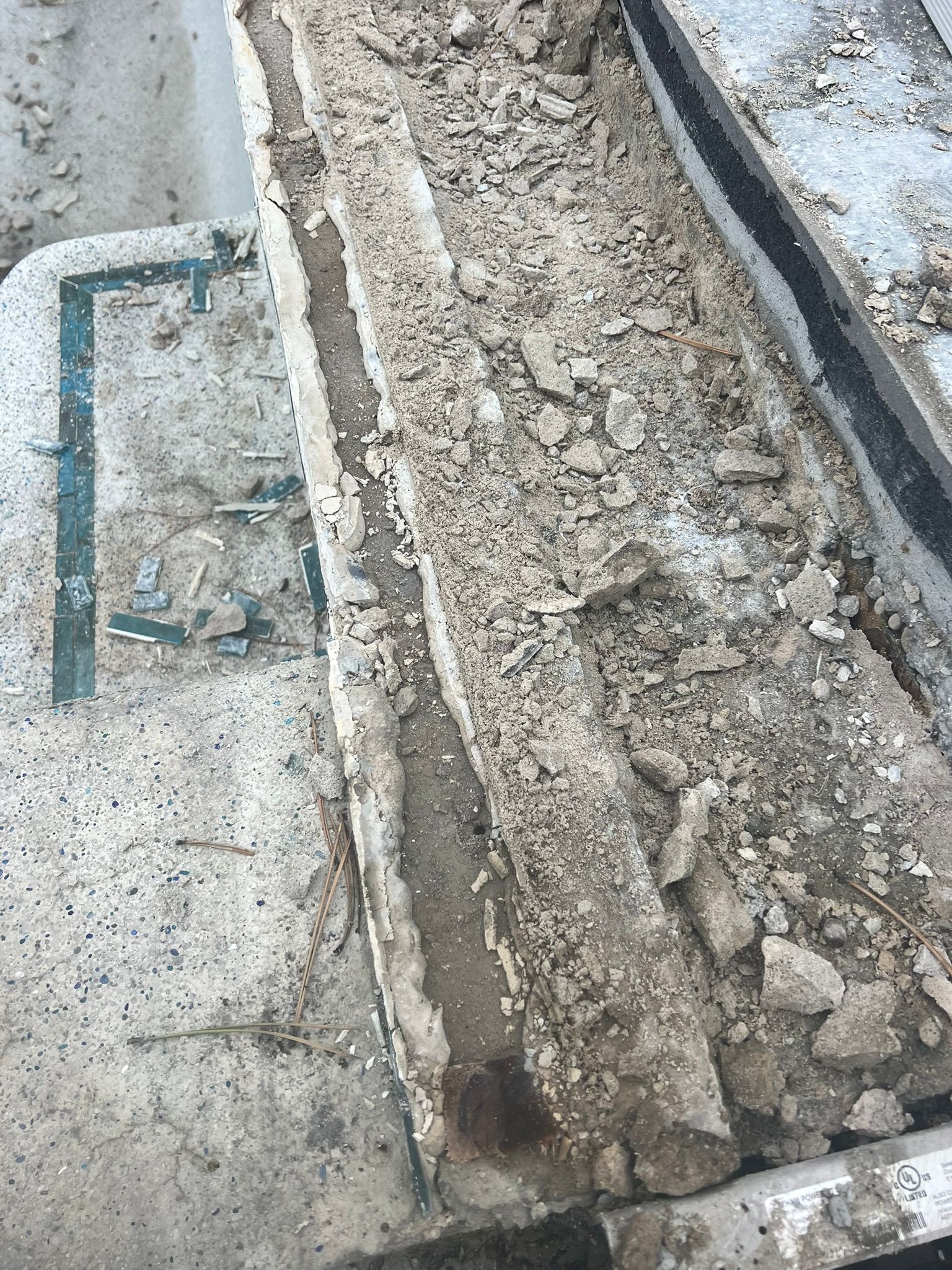 A damaged concrete step with crumbling, loose debris and exposed aggregate surface on a grey exterior staircase.