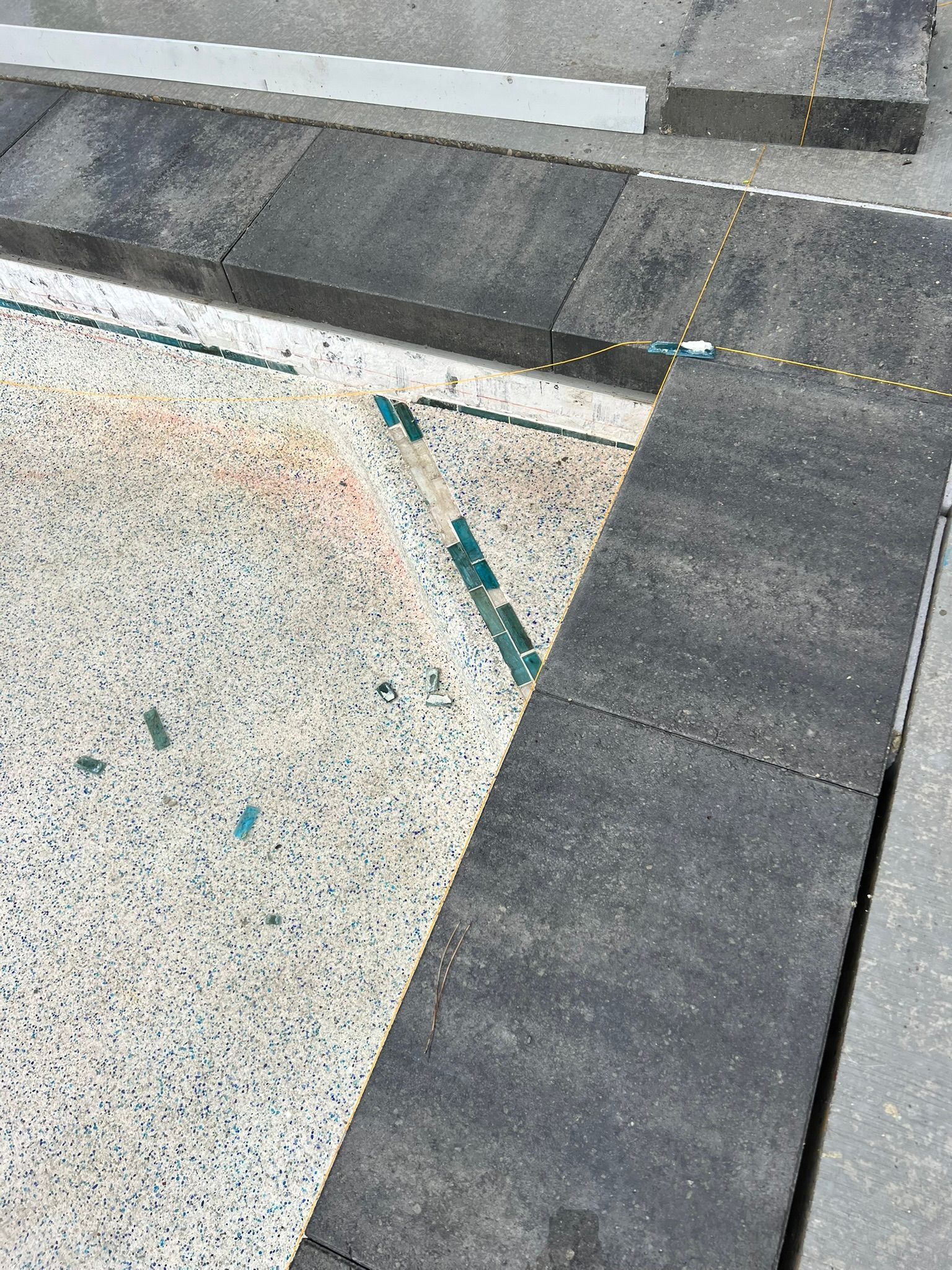 A corner section of a light-colored, speckled surface framed by dark gray, rectangular stone pavers.