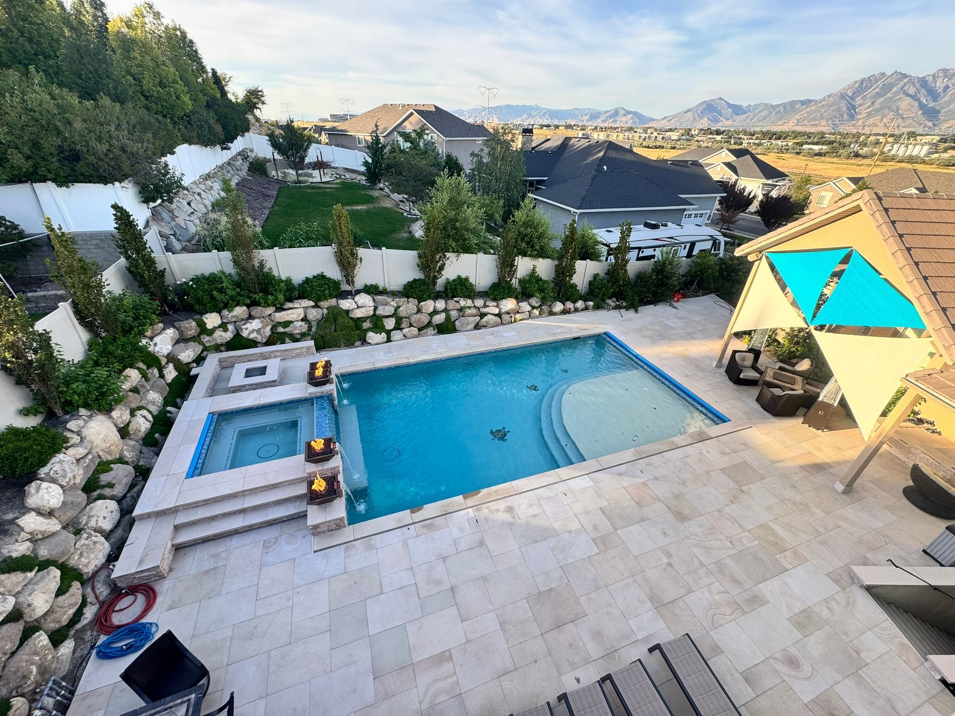 A backyard patio featuring a swimming pool and hot tub, surrounded by stone landscaping and a view of distant mountains.
