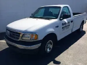 White Ford F-150 pickup truck with company logo on the door parked outside on a sunny day.