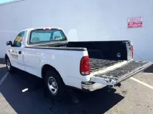 White Ford pickup truck with the tailgate open, parked in a parking lot.