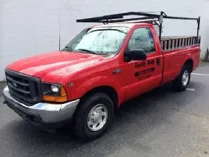 Red Ford pickup truck with ladder rack and sideboards, parked outside.