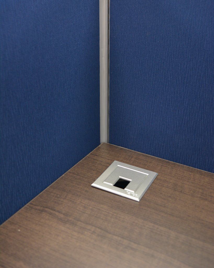 a silver grommet on a desk with blue cubicle panels