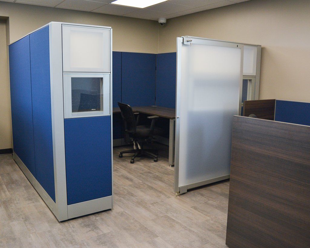 a blue cubicle with sliding door, a desk and a chair