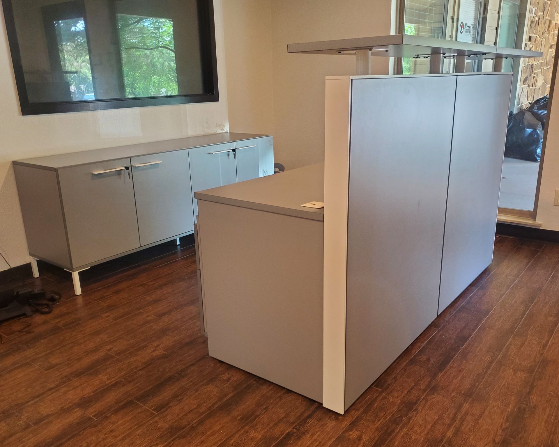 A light gray and white reception desk with storage cabinet behind in a small office.