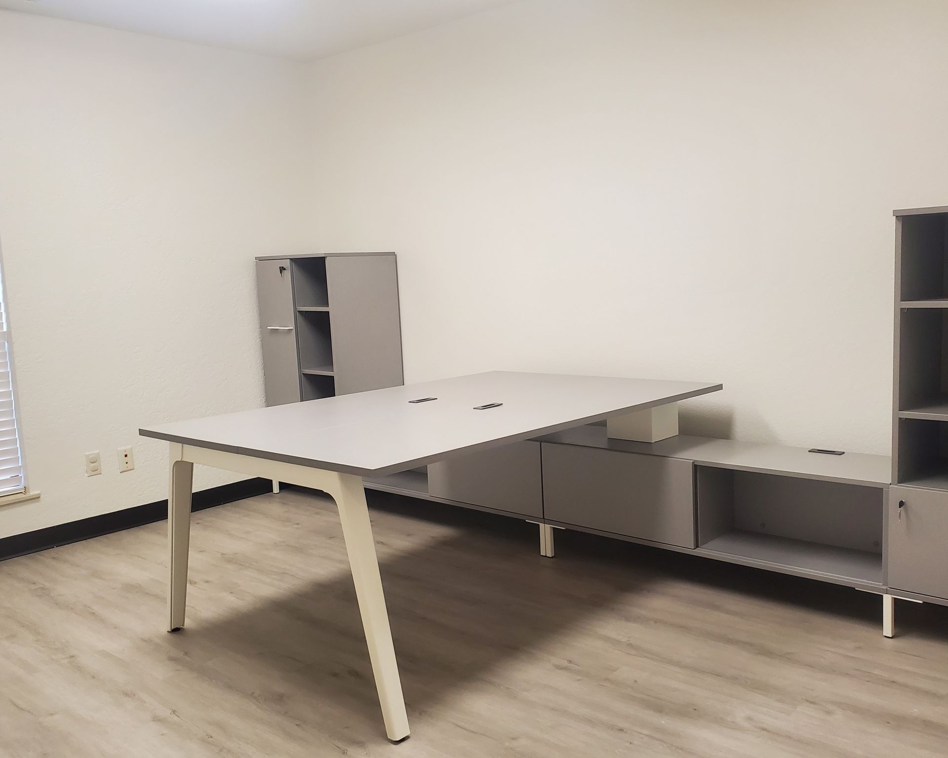 A light gray & white modular desk setup with shared worksurface and mixed storage along the wall.