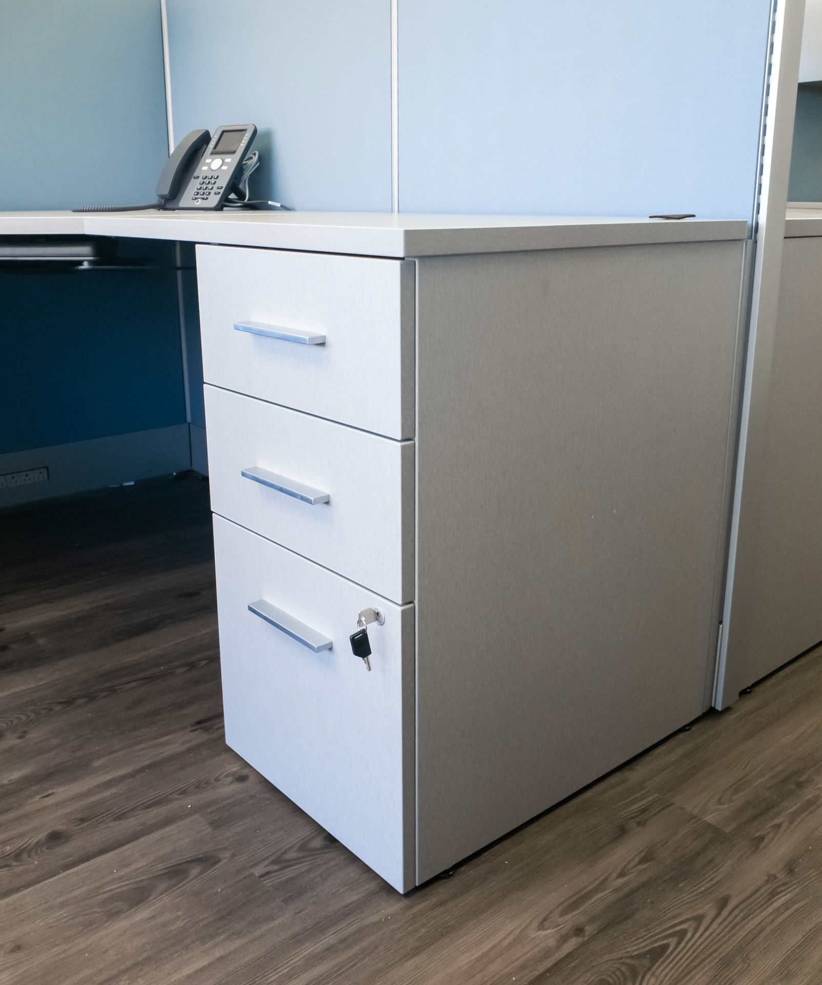 A white desk with three drawers and a phone on it