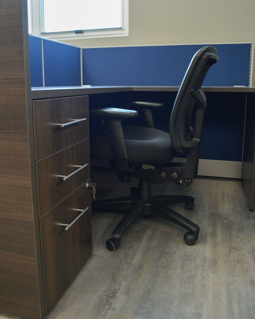 a cubicle with a black chair and a blue divider