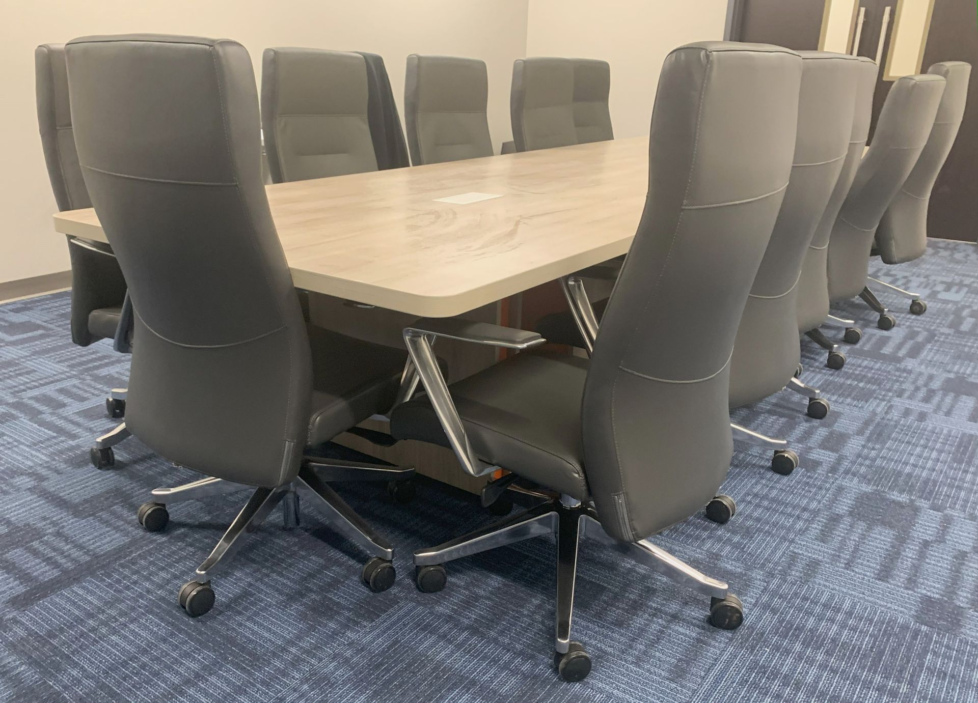 Conference room with a light wood table and gray office chairs on a blue patterned carpet.