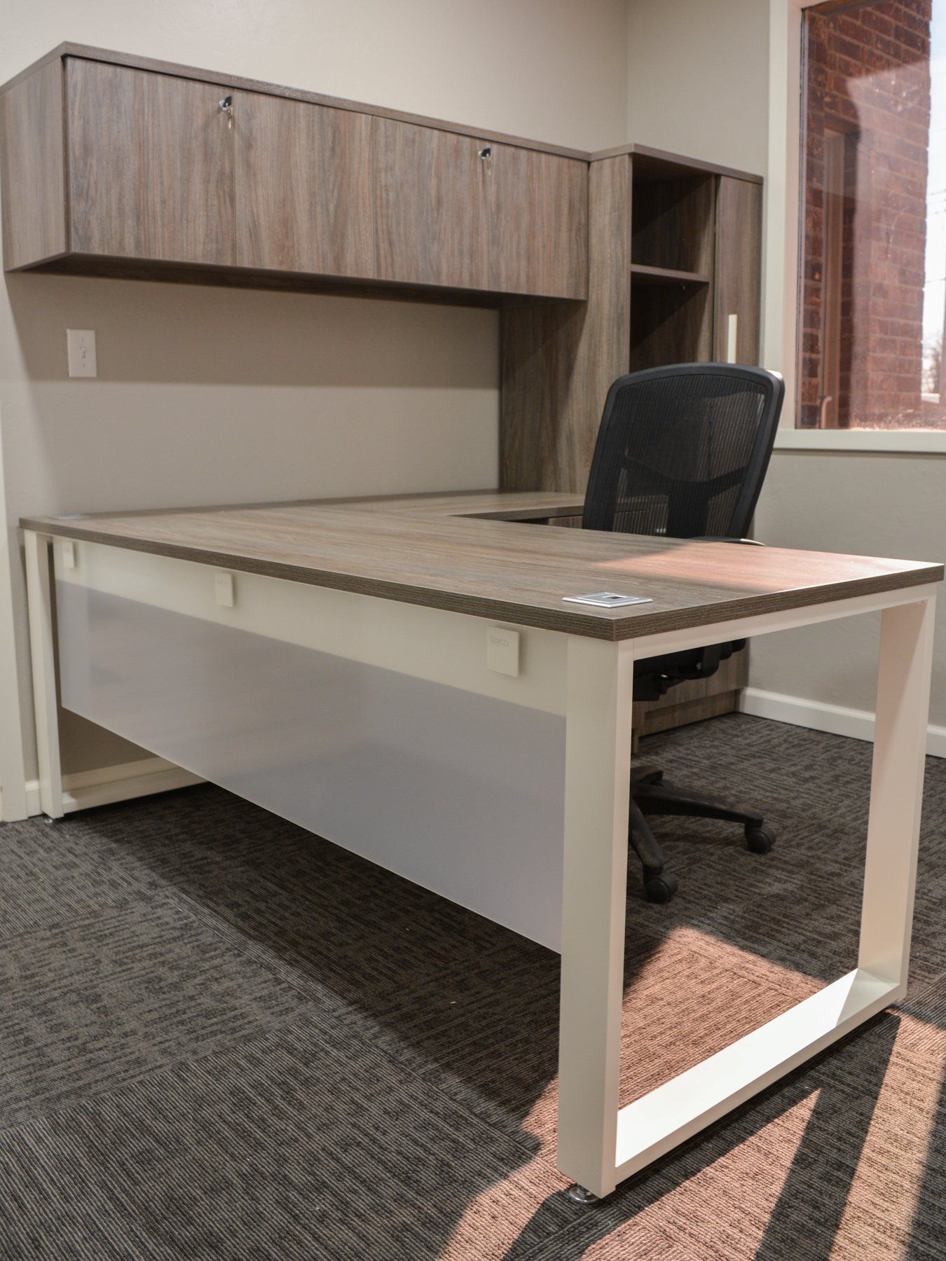laminate L shape desk with a white frame and a black chair in an office
