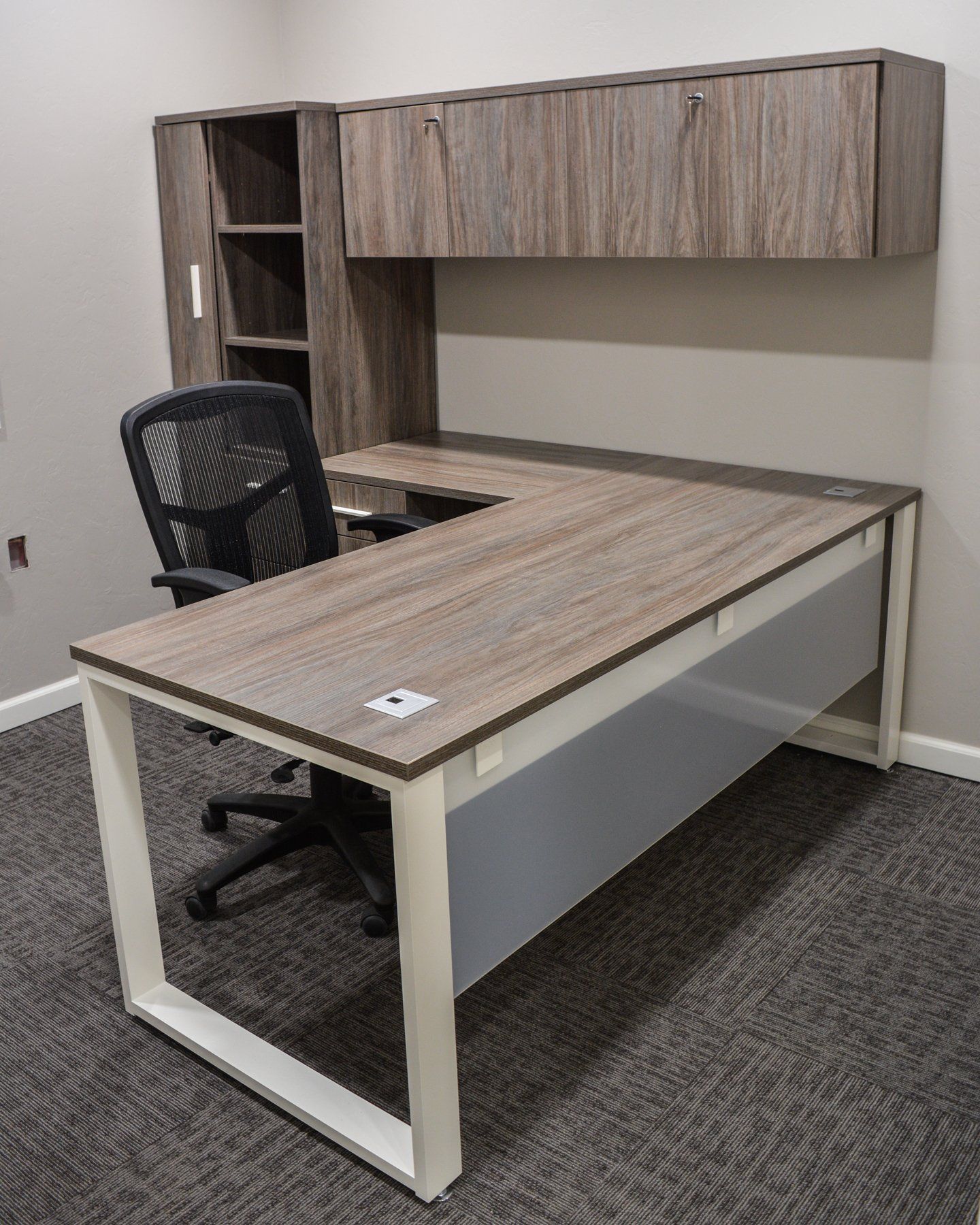 laminate L shape desk with a white frame and a black chair in a small office