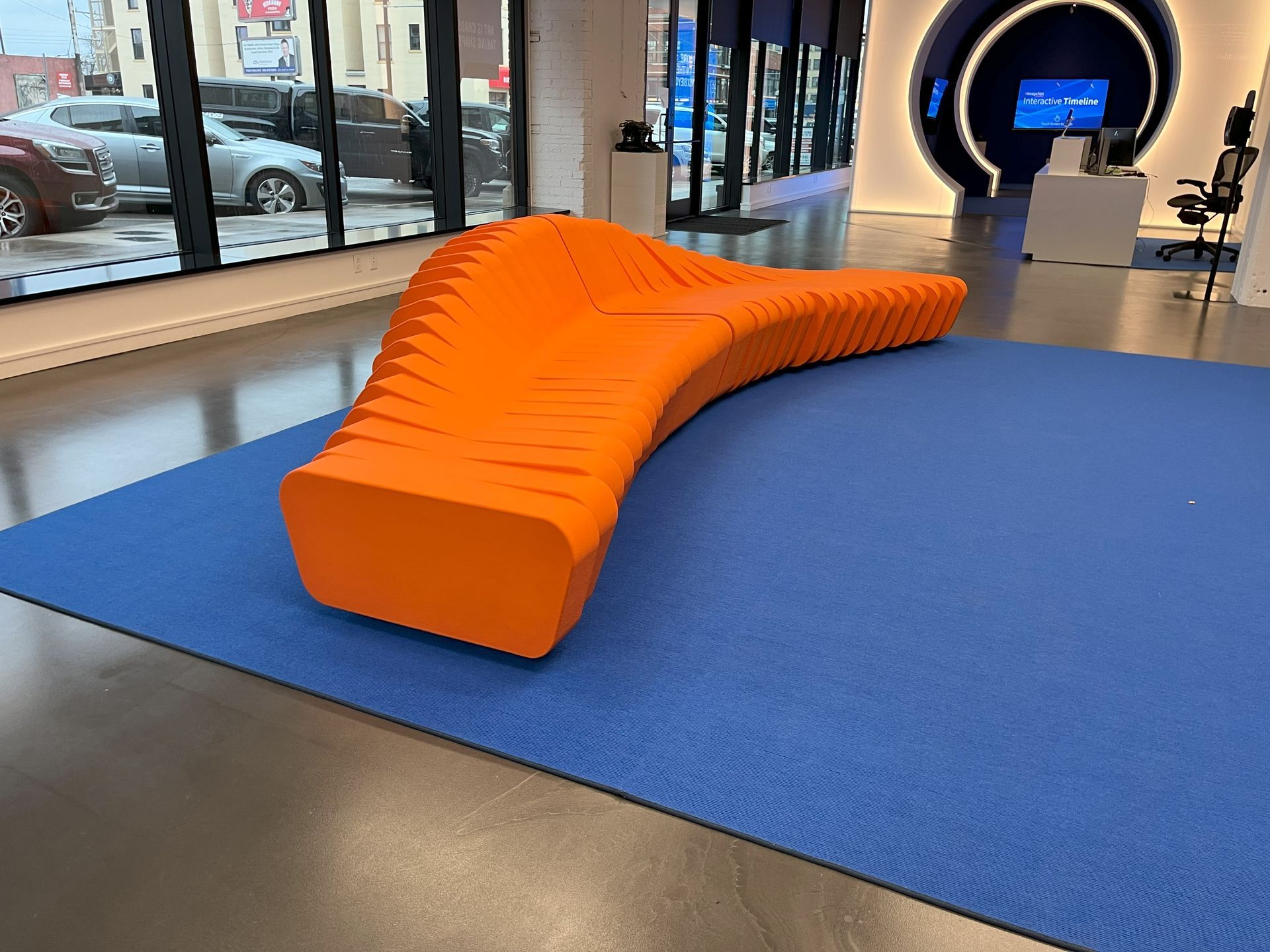 Cliffy modern orange modular sofa on blue rug with windows and cars in background.