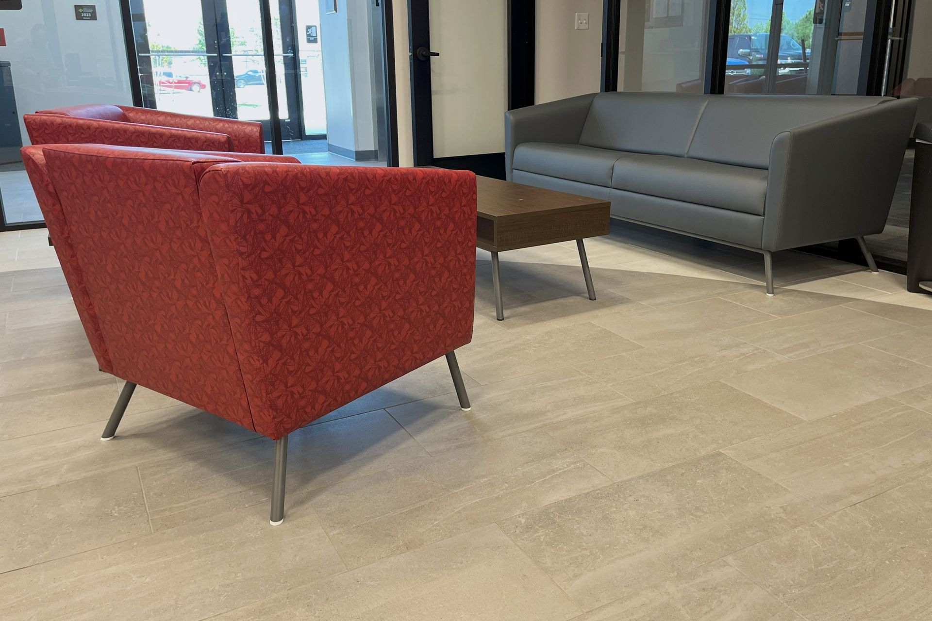 Lobby with red and gray furniture, wood table, and light tile floor.  Window in the background.