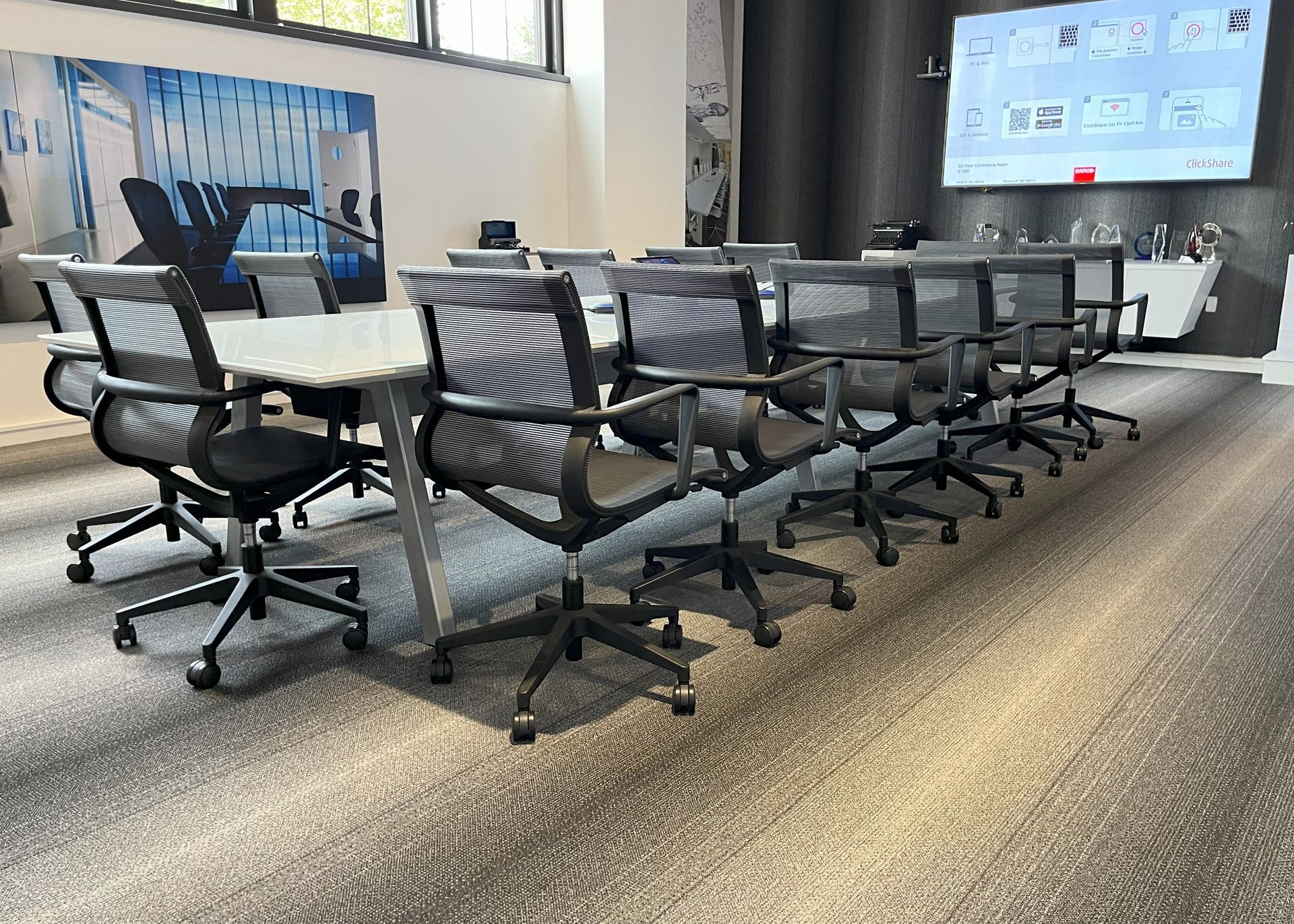 White and silver rectangular conference table with dark gray mesh chairs on gray striped carpet.