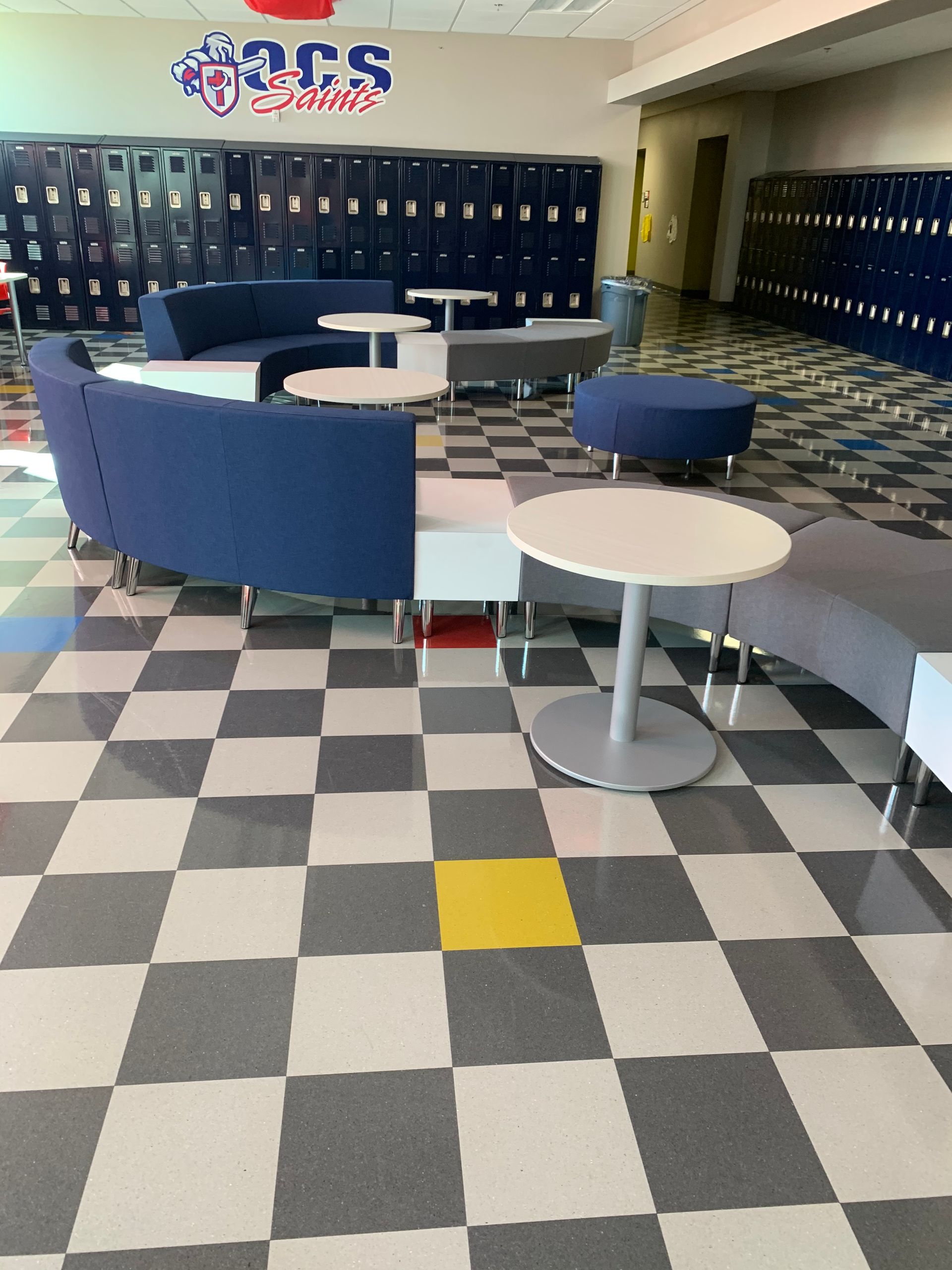 Modular gray sofa with blue partial back and white tables on gray checkered floor.