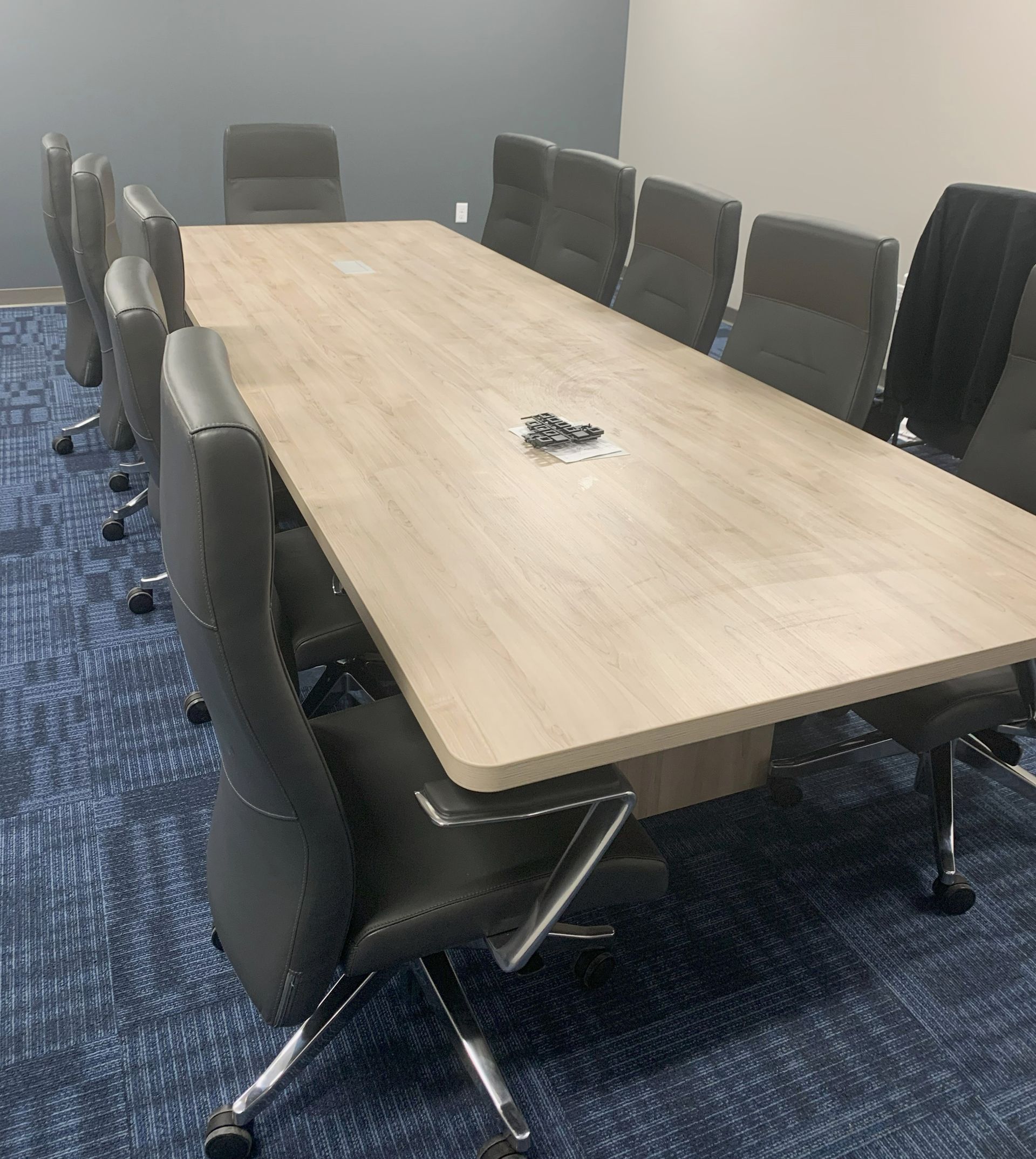 Conference room with large wooden table, dark leather chairs, and blue carpet.