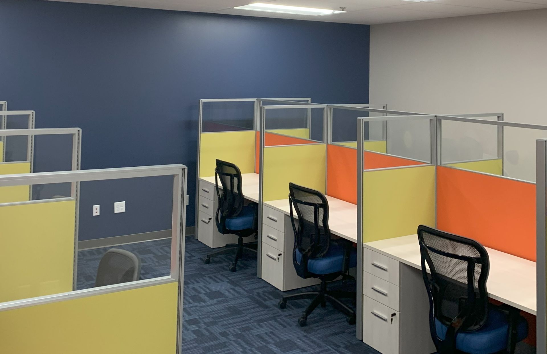 Office cubicles with yellow and orange dividers, blue carpet, blue and gray walls.
