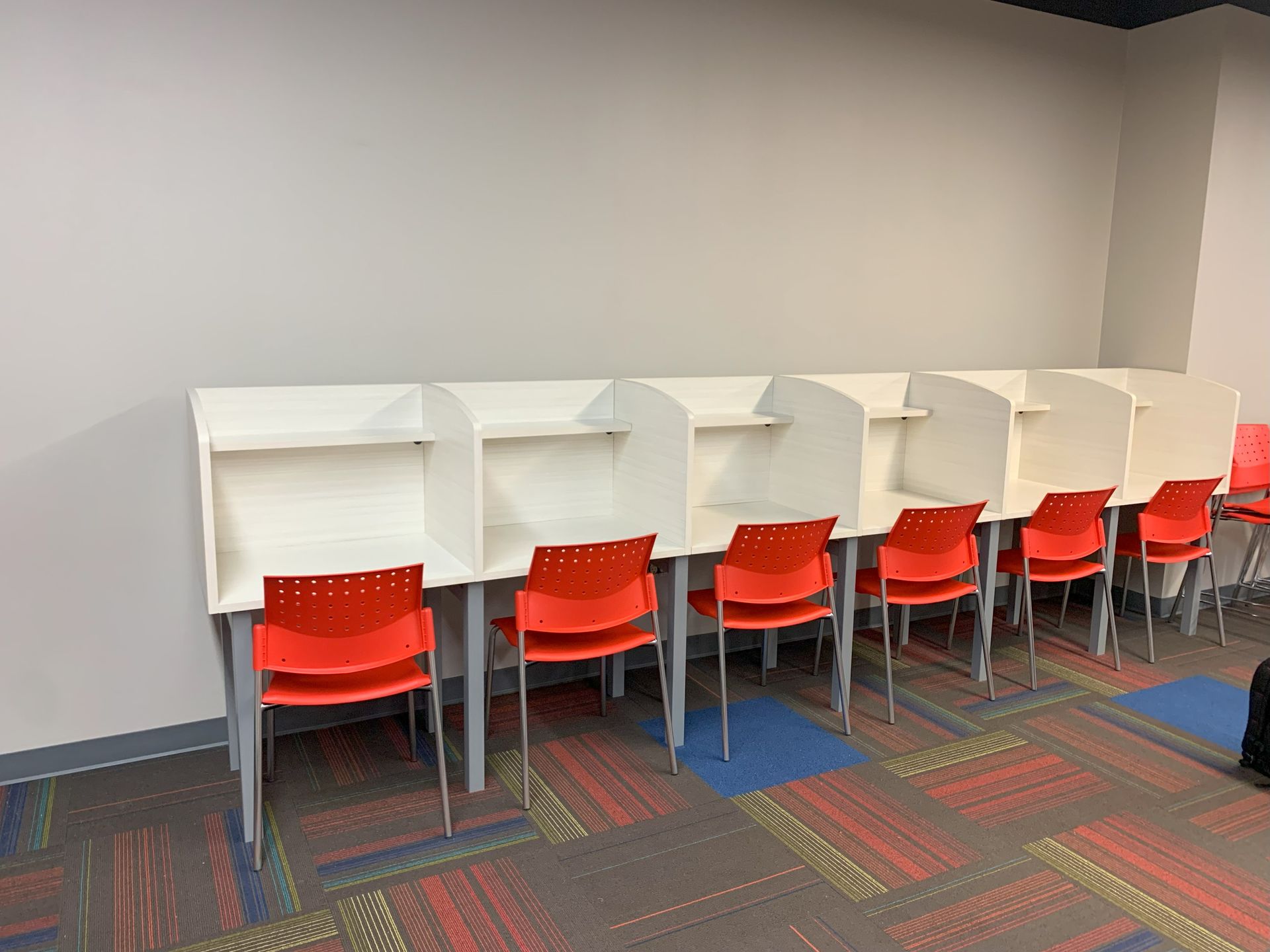 Row of white study carrels with red plastic chairs against light gray wall.