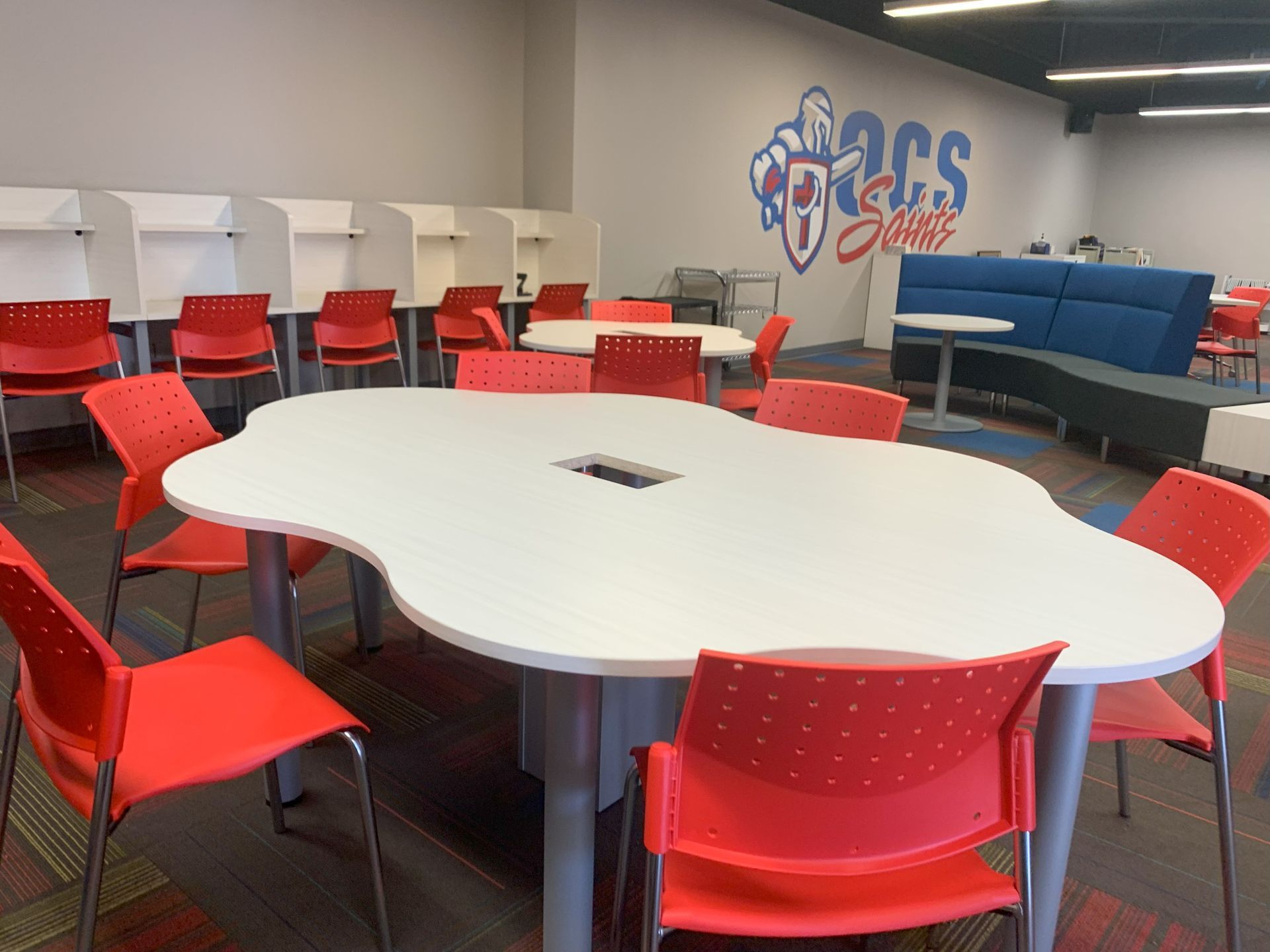 White oval student table with bright red chairs; white study carrels with more red chairs behind.