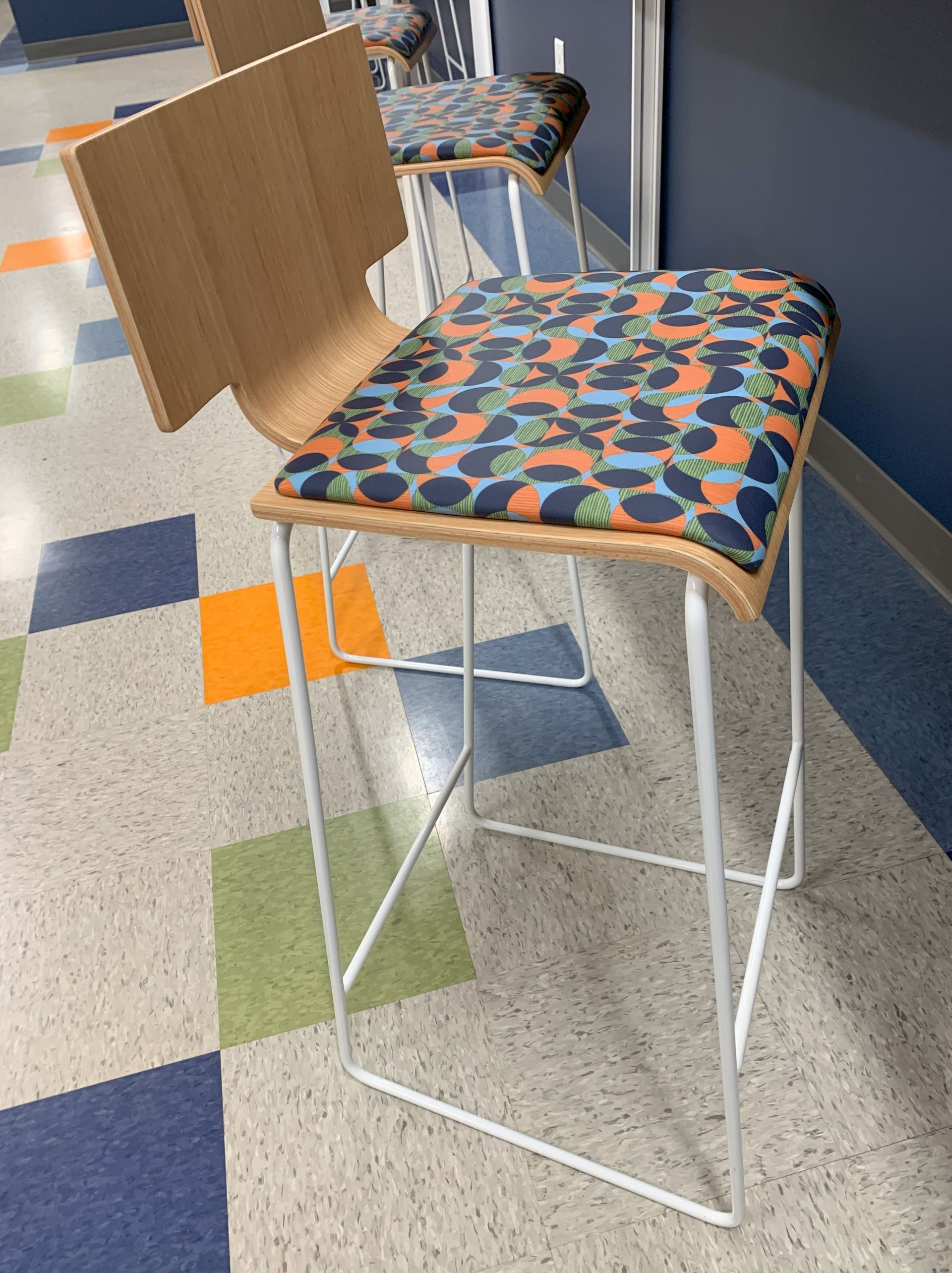 Bar stool with a patterned seat and light wood back, set in a tiled hallway.