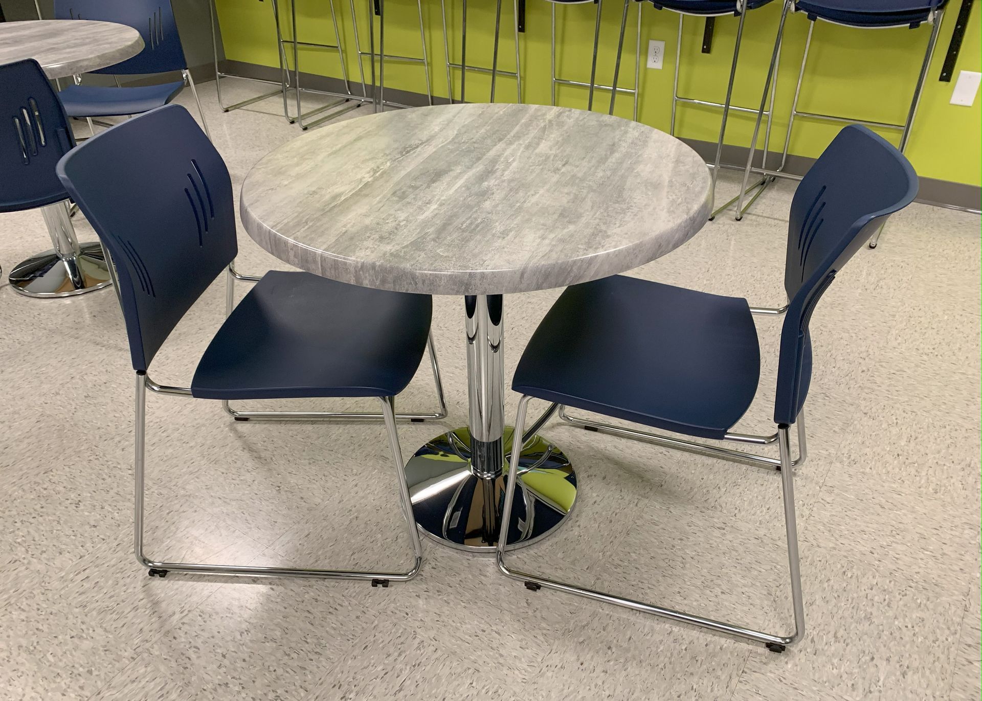 Round table with two blue chairs in a room, chrome legs and a light marble top.