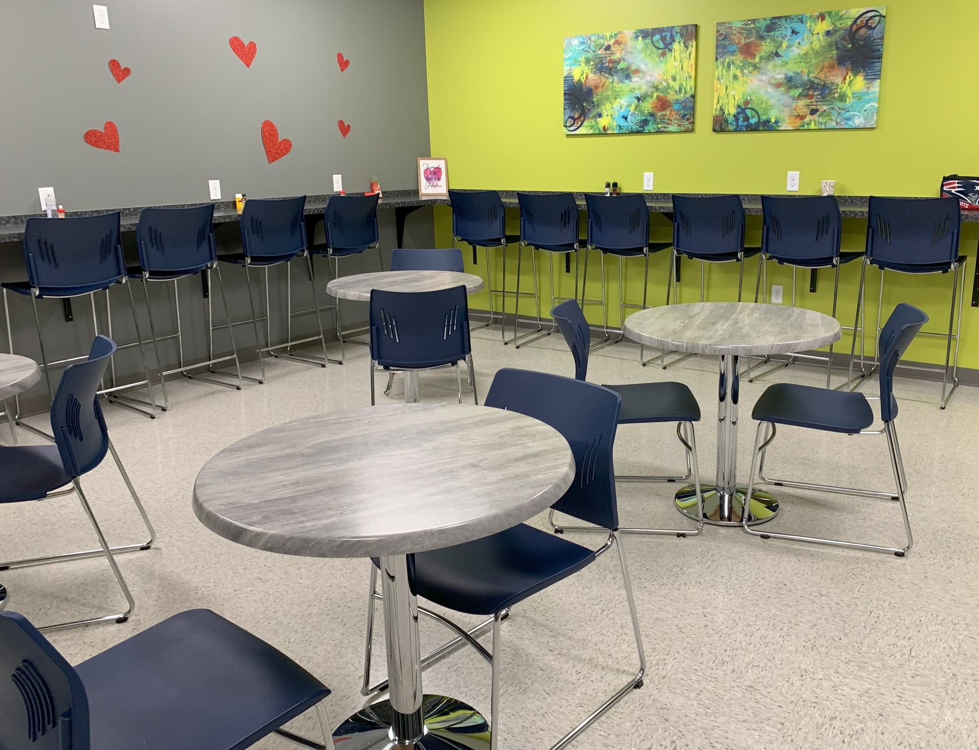 Empty break room with gray tables, blue chairs, and bar seating against green and gray walls.