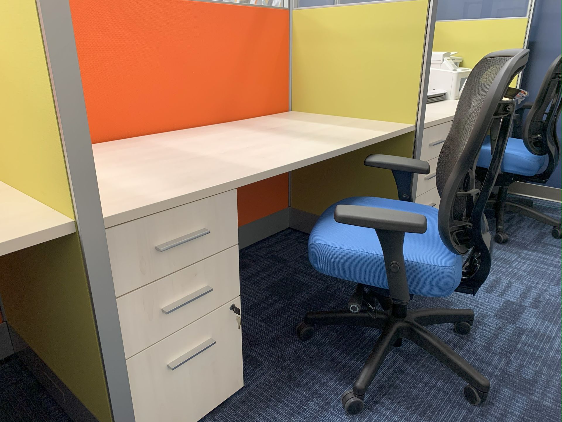 Small workstation desk with blue office chair, orange and green panels, in an office setting.