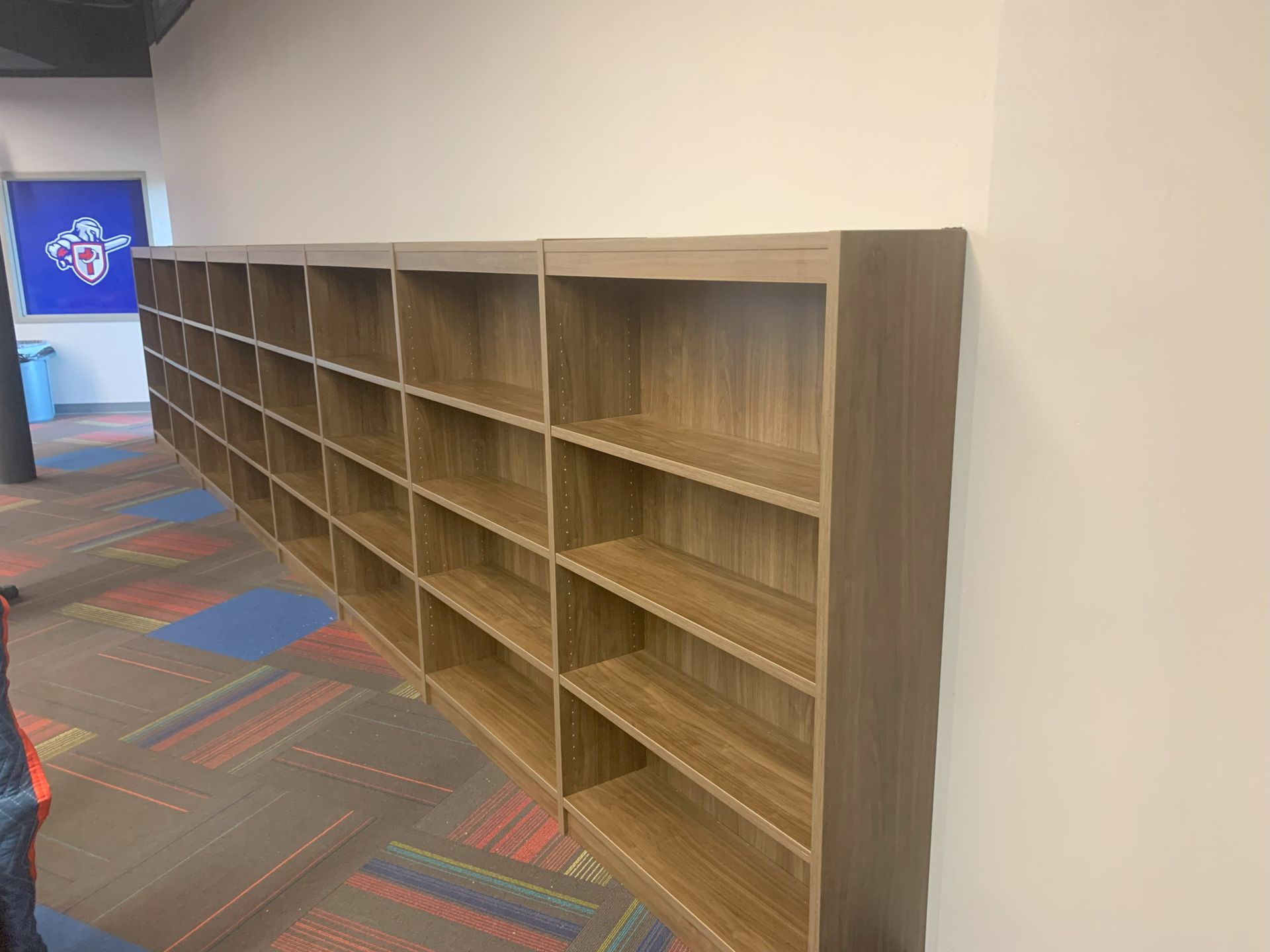 Long row of laminate woodgrain bookcases against a gray wall on the right side of a large room.