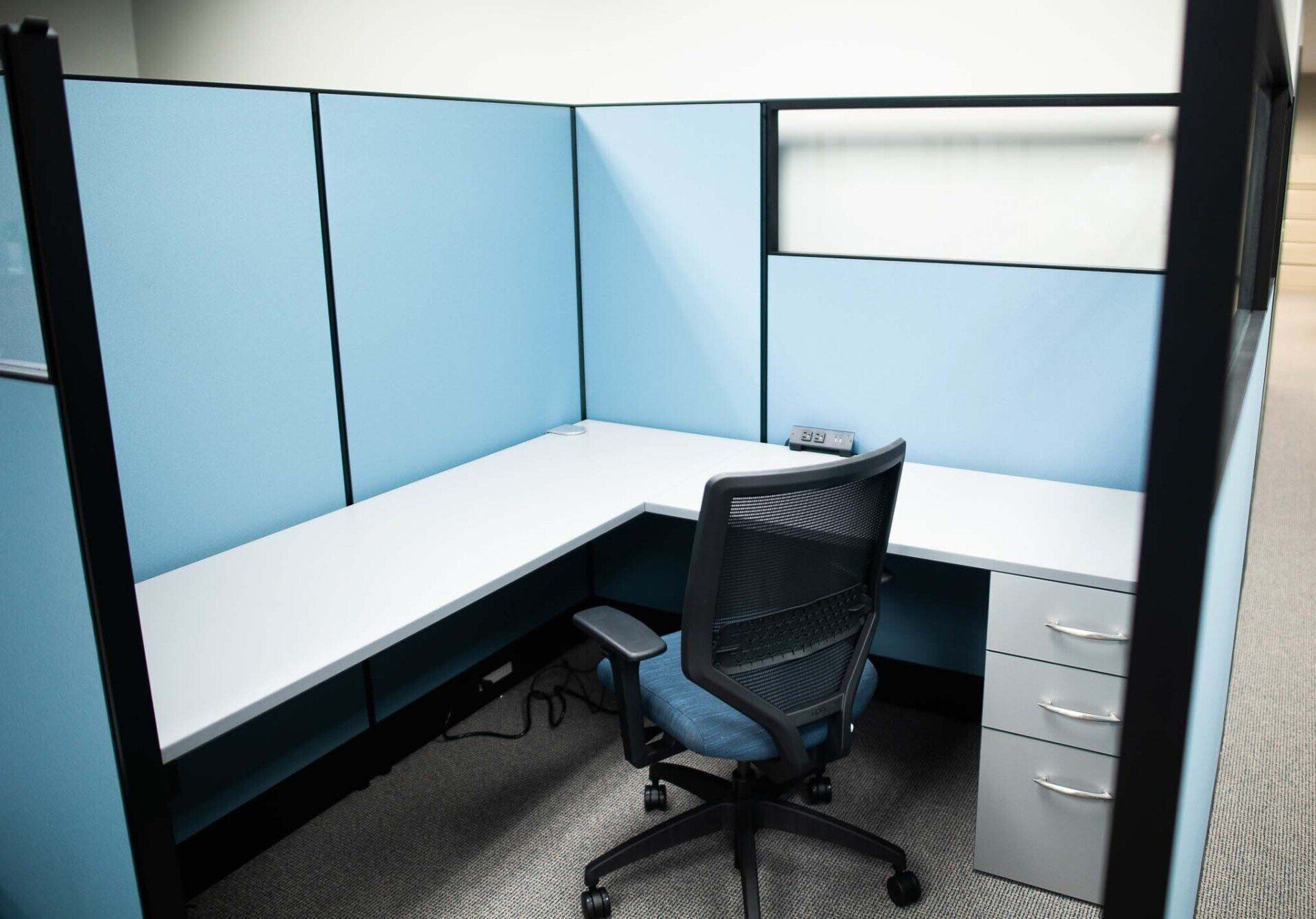 a light blue office cubicle with a chair and a desk