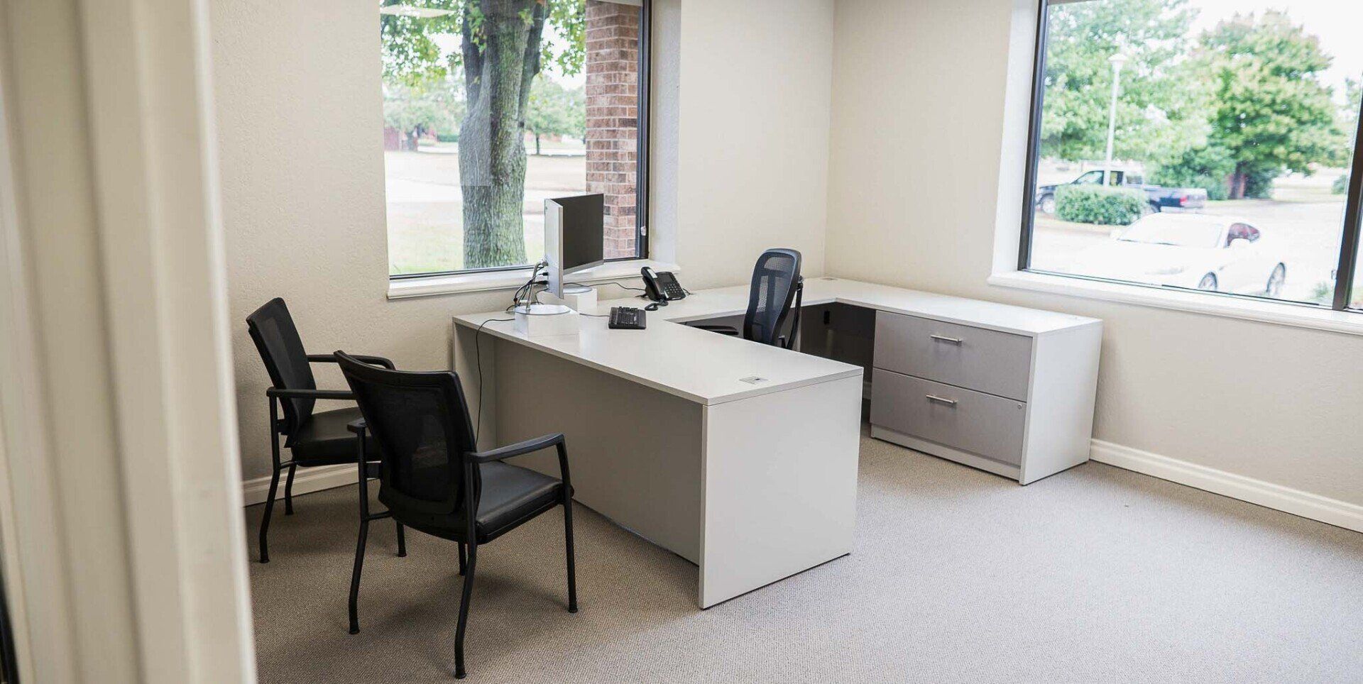 a small office with a white U shape desk and two chairs in front