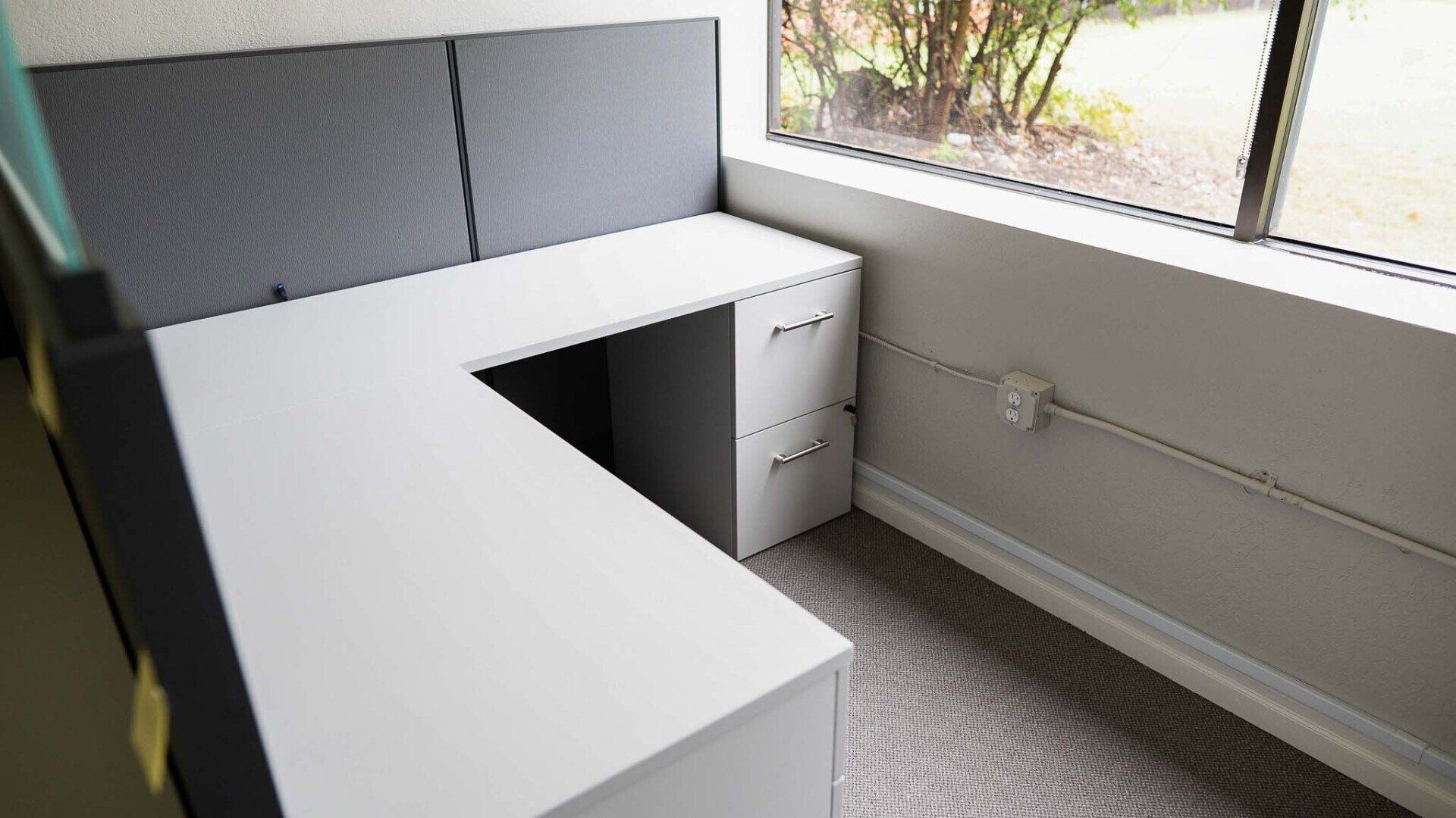 a cubicle with a desk and drawers and a window