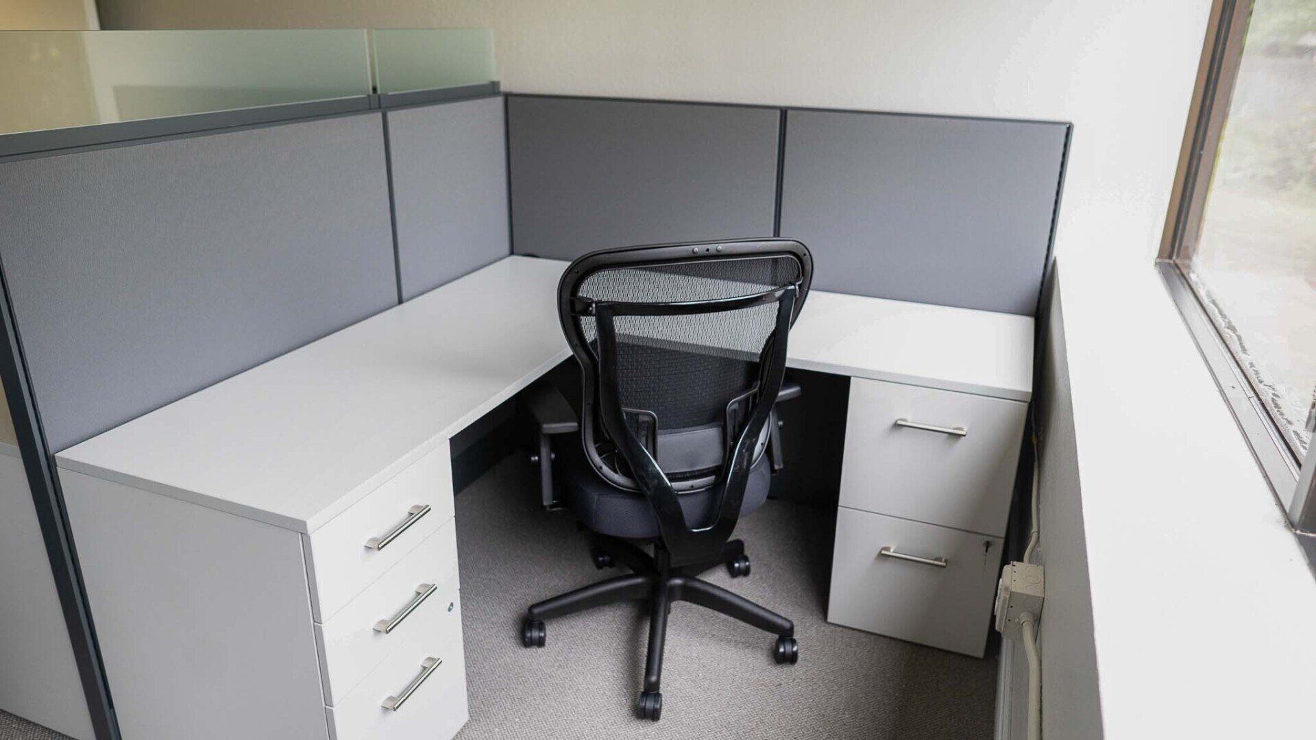 an office cubicle with a black chair and a window