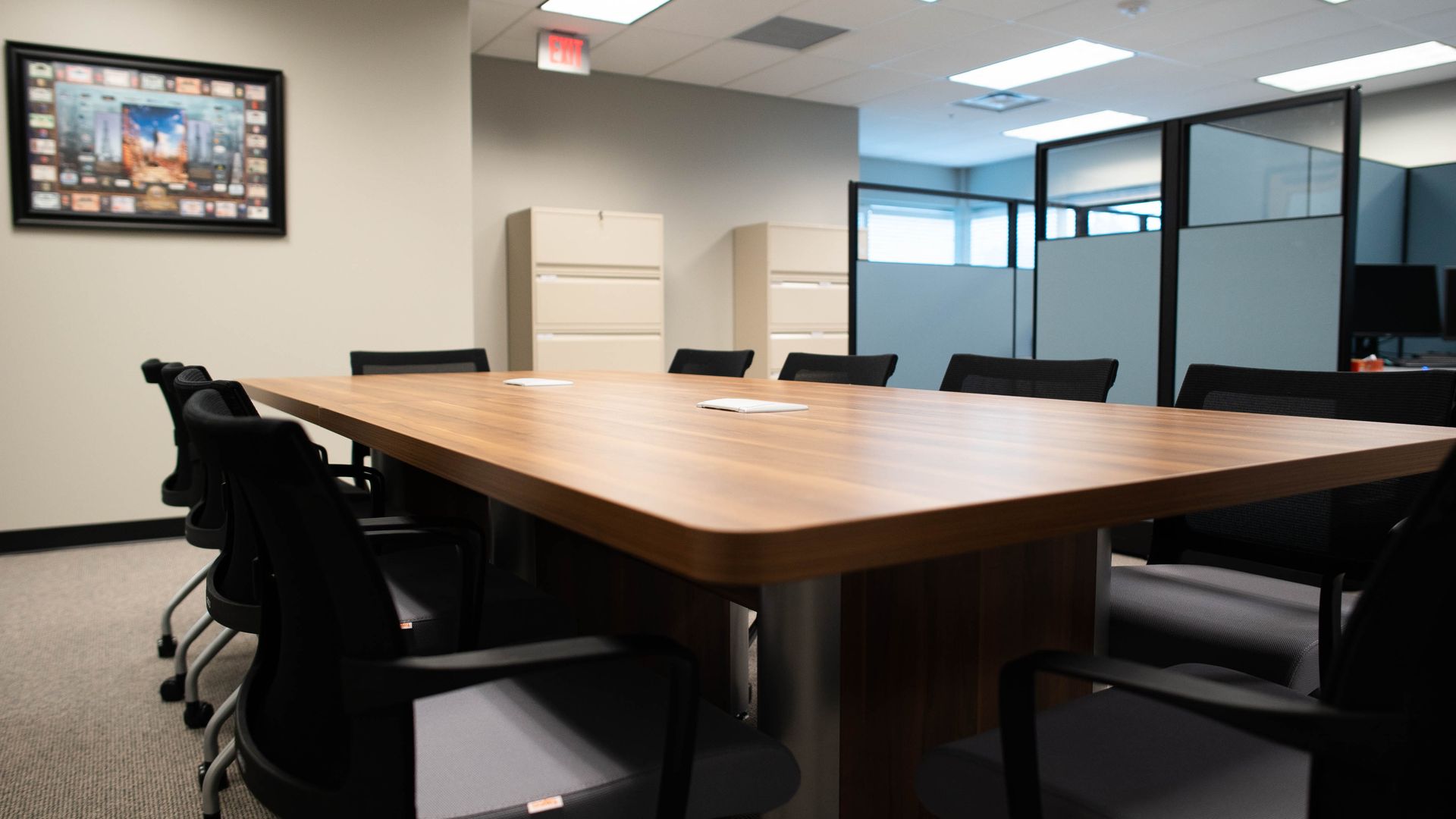 A conference room with a rectangular woodgrain table and chairs, blue cubicles behind