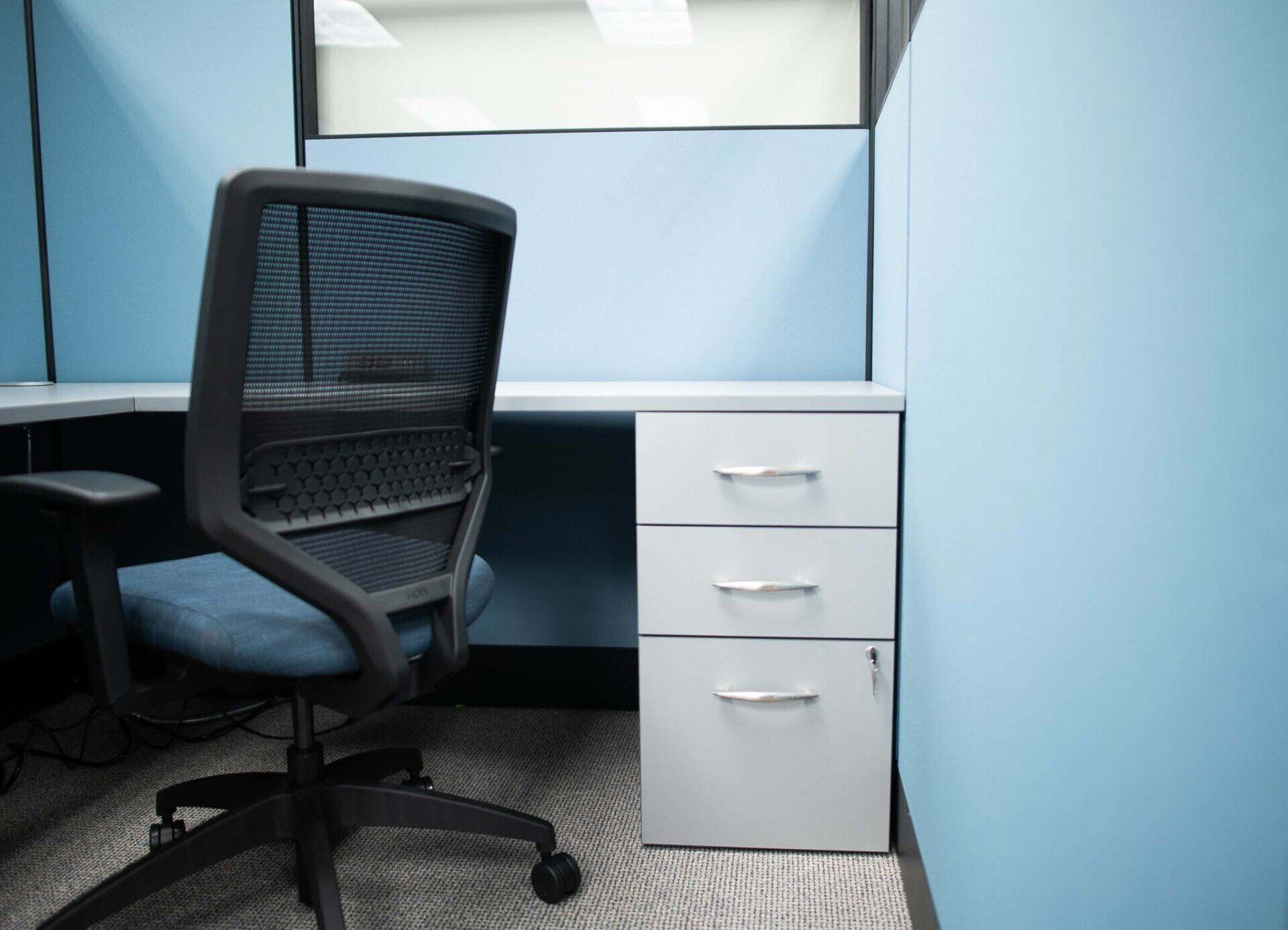 a cubicle with a chair and a filing cabinet