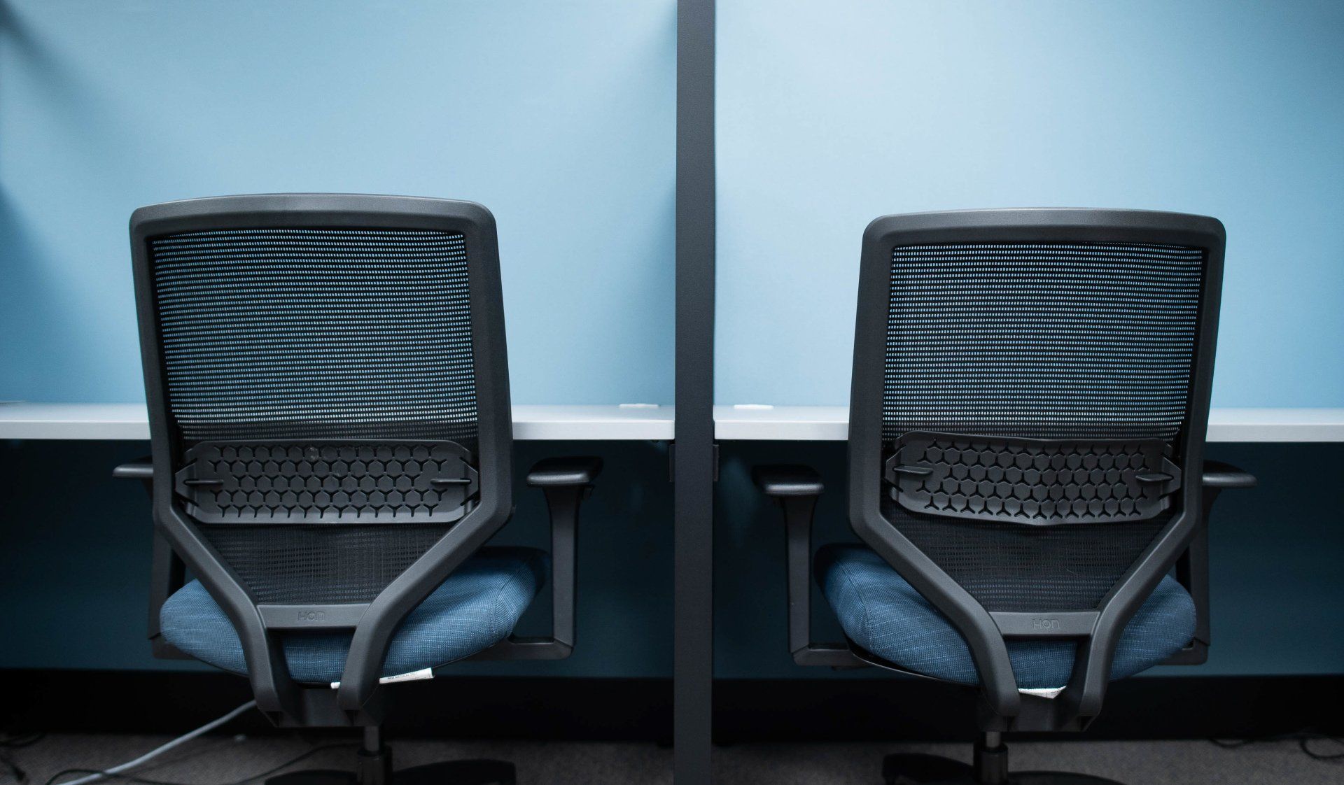 Two office chairs are sitting next to each other in blue cubicles.