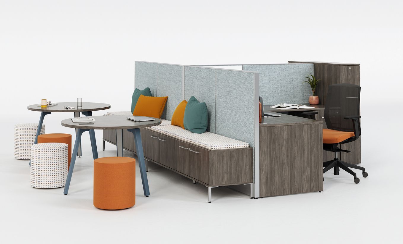 Two round tables with colorful ottomans and a long bench sit against a gray cubicle wall.