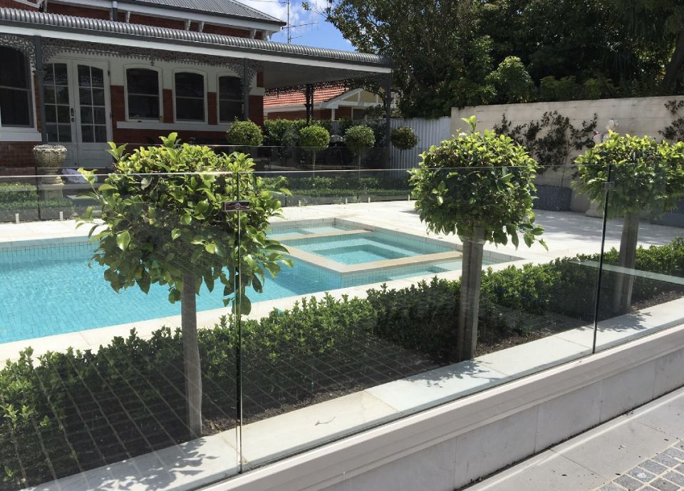 View of an outdoor pool with plants and glass fence