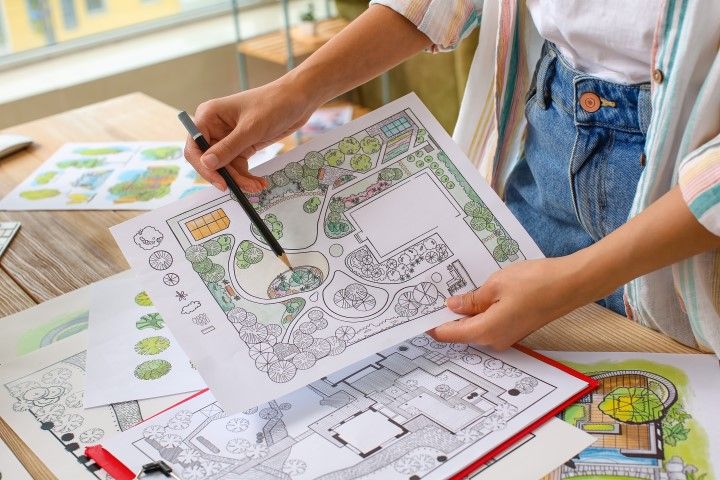 Hands reviewing landscape design plans over a table with sketches and colored site drawings