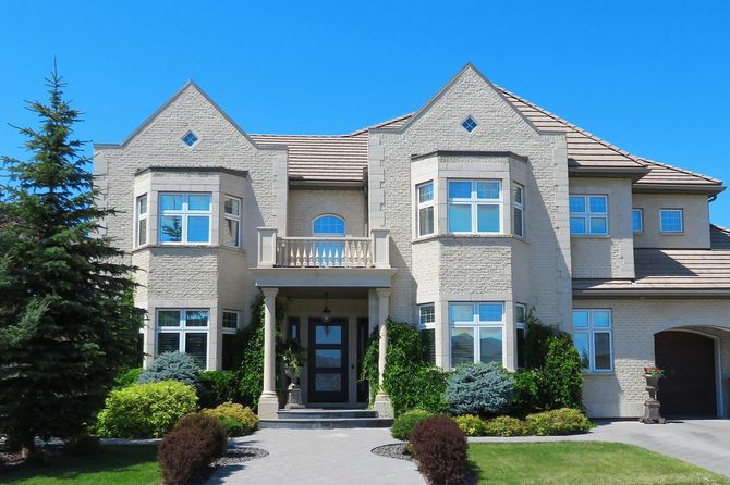 Large modern two-story stone house with blue-trimmed windows and a manicured front lawn