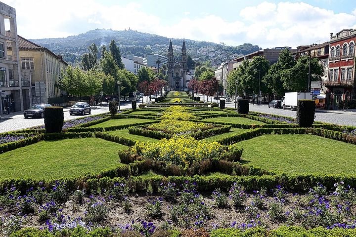 Formal garden with geometric hedges, flowers, and a tree-lined boulevard with mountains in the background