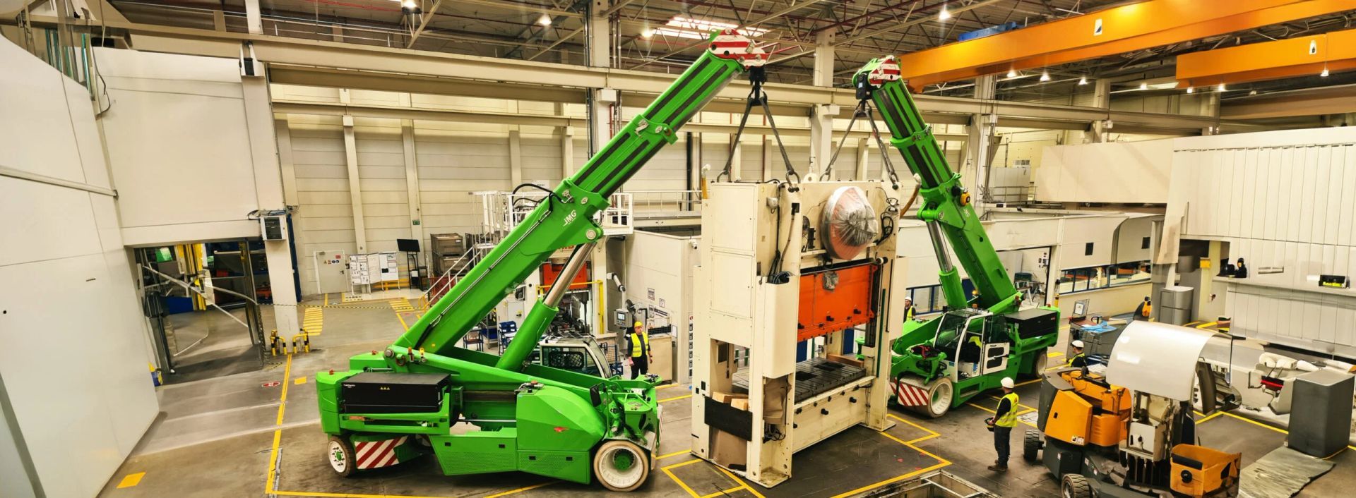 Una gru JMP elettrica sta sollevando un grande macchinario in una fabbrica.