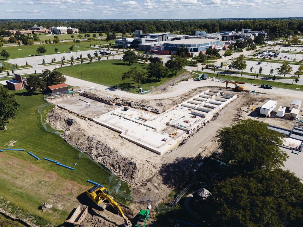 Aerial view of a large construction site with concrete foundations, heavy machinery, and nearby roads.