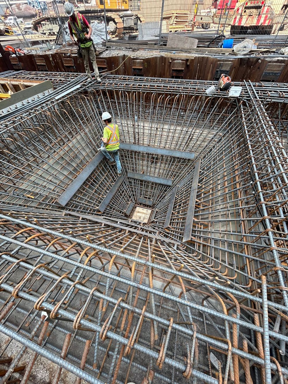 Construction worker in yellow vest standing in a deep rebar foundation pit at a building site