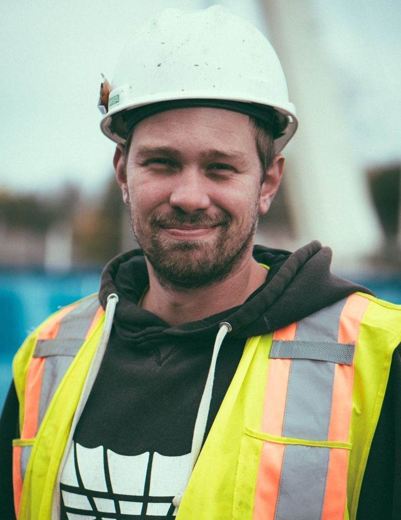 Construction worker in a white hard hat and reflective vest, smiling outdoors at a job site