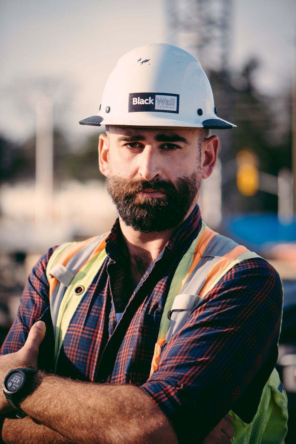 Construction worker in hard hat and safety vest with arms crossed at a work site