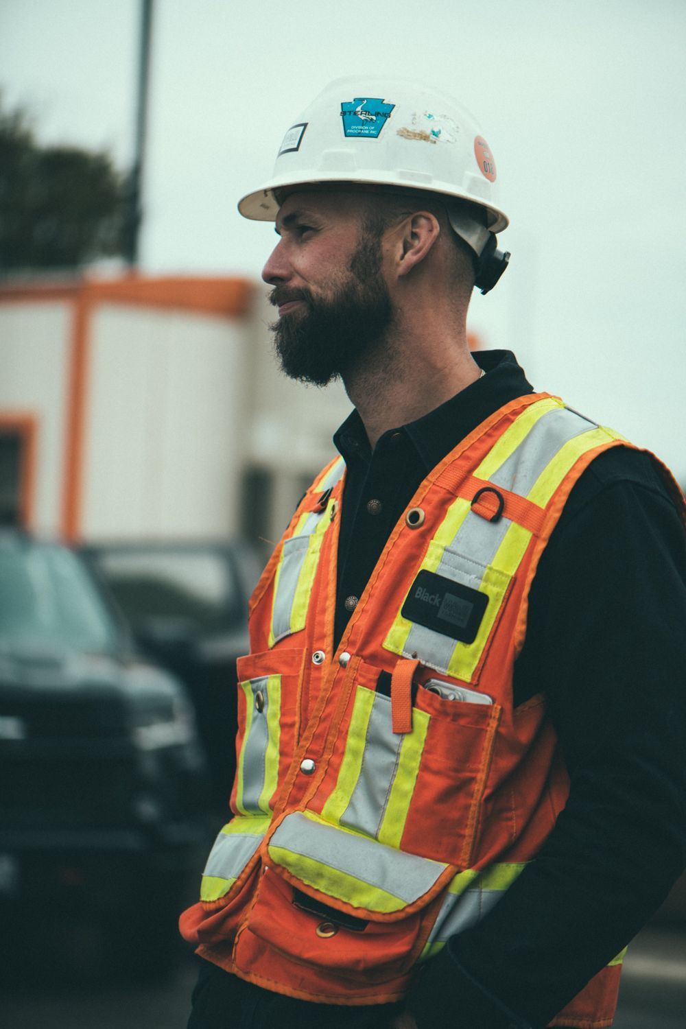 Construction worker in white hard hat and orange safety vest standing outdoors at a job site.