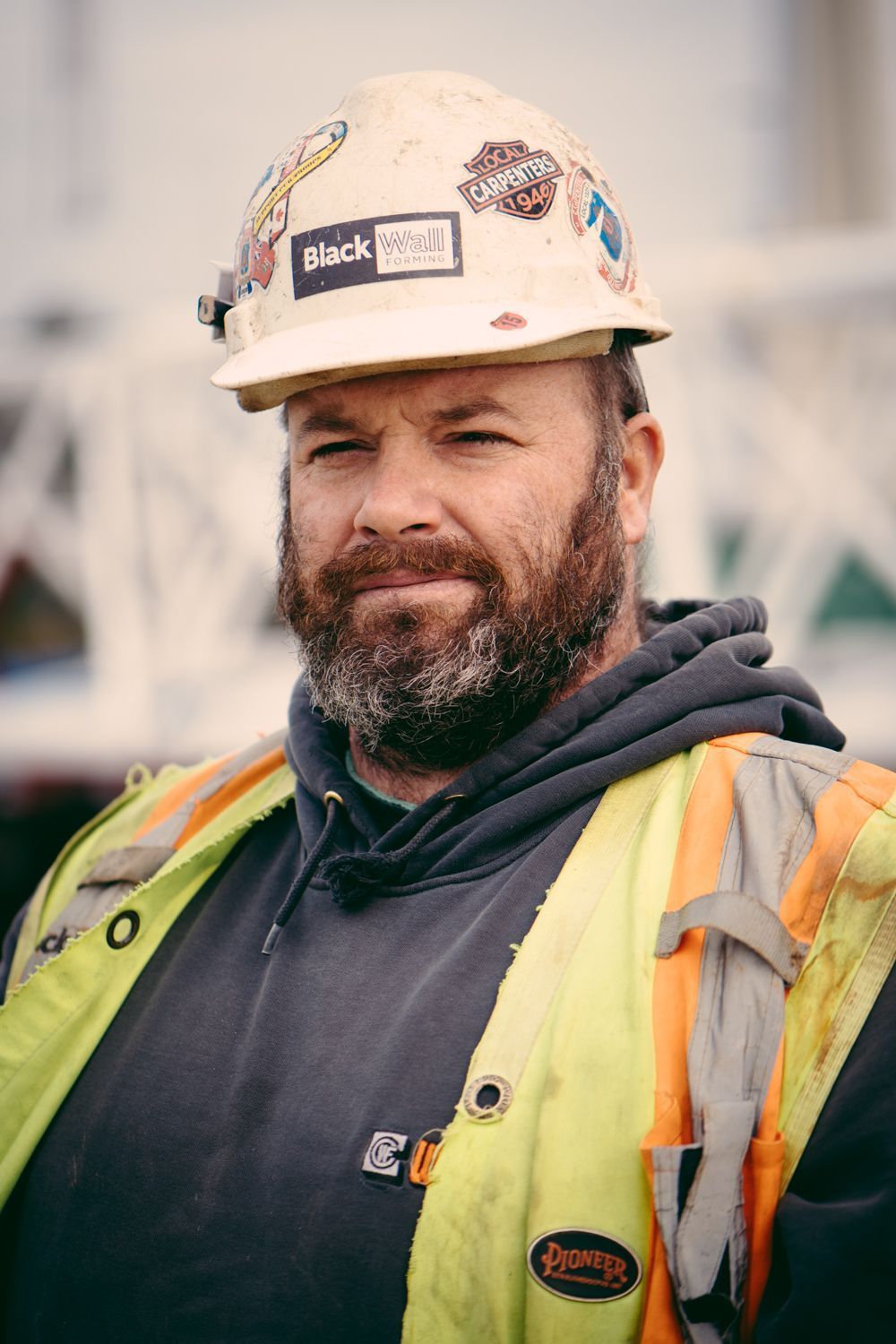 Construction worker in hard hat and safety vest, standing outdoors with a slight smile